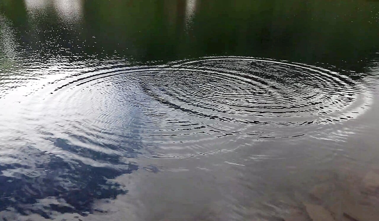 Interfering waves on water. The alternating reinforcement and cancellation is the signature of wave behaviour, and it is what the two-slit pattern demonstrates.