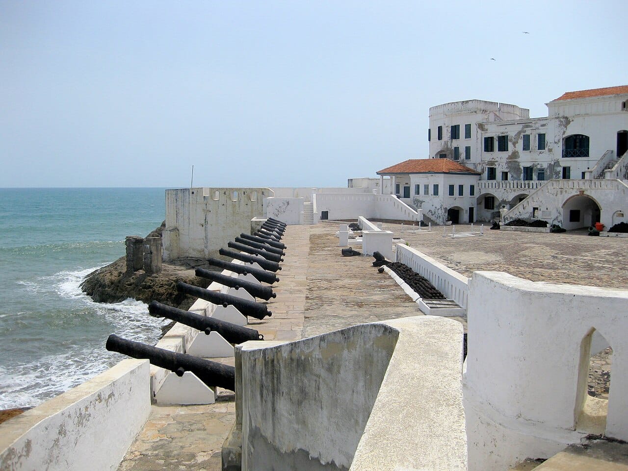 Cape Coast Castle, the former seat of British colonial administration on the Gold Coast. Beneath its whitewashed courtyards lie the dungeons where captives were held before embarkation, and the castle is now a museum and a place of return for visitors from the African diaspora.