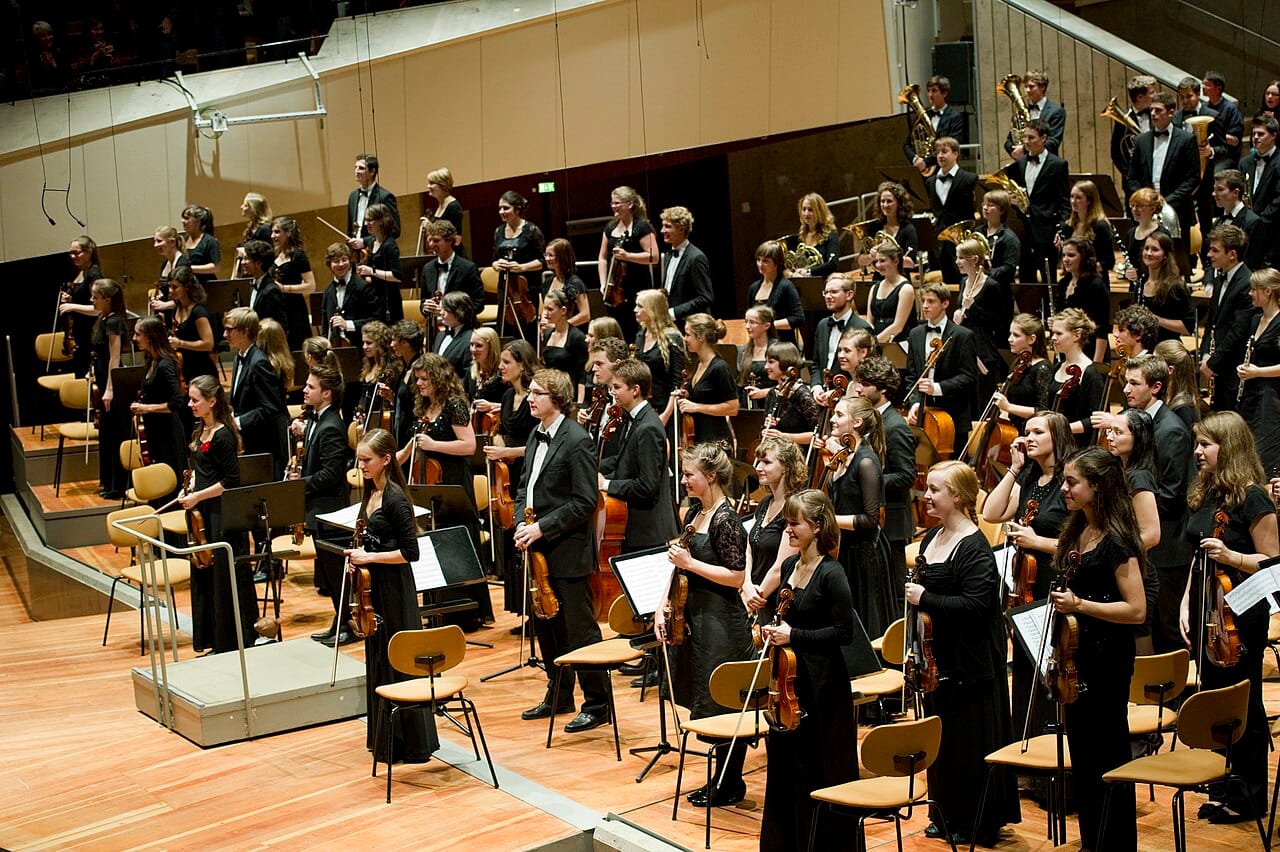 An orchestra in performance. Sustained musical training shows small measured associations with cognitive outcomes; passive listening, which is what the Mozart effect claimed, does not.