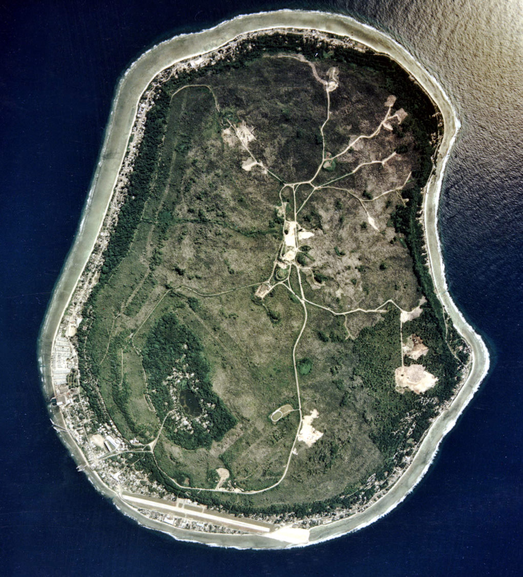 A satellite image of Nauru. The pale, scarred interior is the mined-out phosphate plateau, an environmental ruin that fills most of the island, while habitation clings to the thin green coastal ring.
