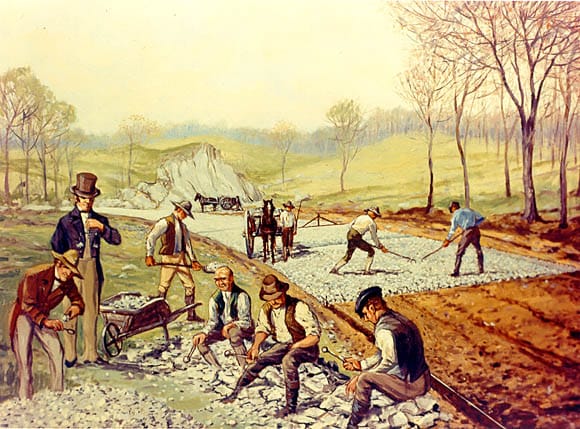An early macadam road under construction. The insight was that a road can be built of small angular stones that lock together, on a drained foundation, without heavy masonry beneath.