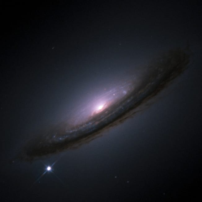 A supernova in a distant galaxy, visible at lower left as a single point rivalling the galaxy's core. The brightness is temporary and the star does not survive.