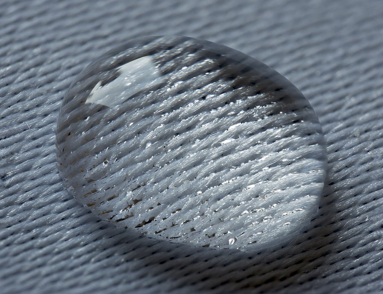 A water droplet resting on woven fabric without soaking through. Whether a liquid wets a surface or beads on it is set by the balance between its cohesion and its attraction to the solid.