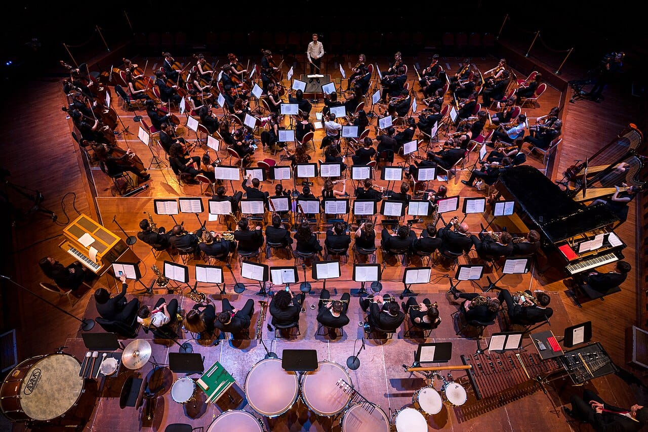 An orchestra from above, arranged so that the conductor is visible to every player. The seating plan is a practical response to the problem of coordinating a large ensemble.